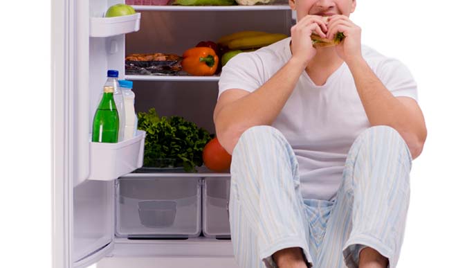 開けっぱなしの冷蔵庫の前で何やら食べている男性