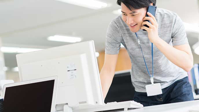 PCを見ながらスマホで連絡する社員