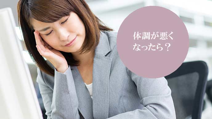 会社のデスクで、こめかみを指で押さえて疲れた表情の女性
