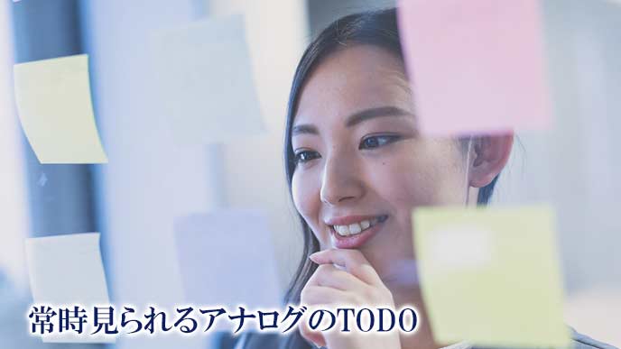 メモ付箋を透明ボードに貼って整理する女性社員